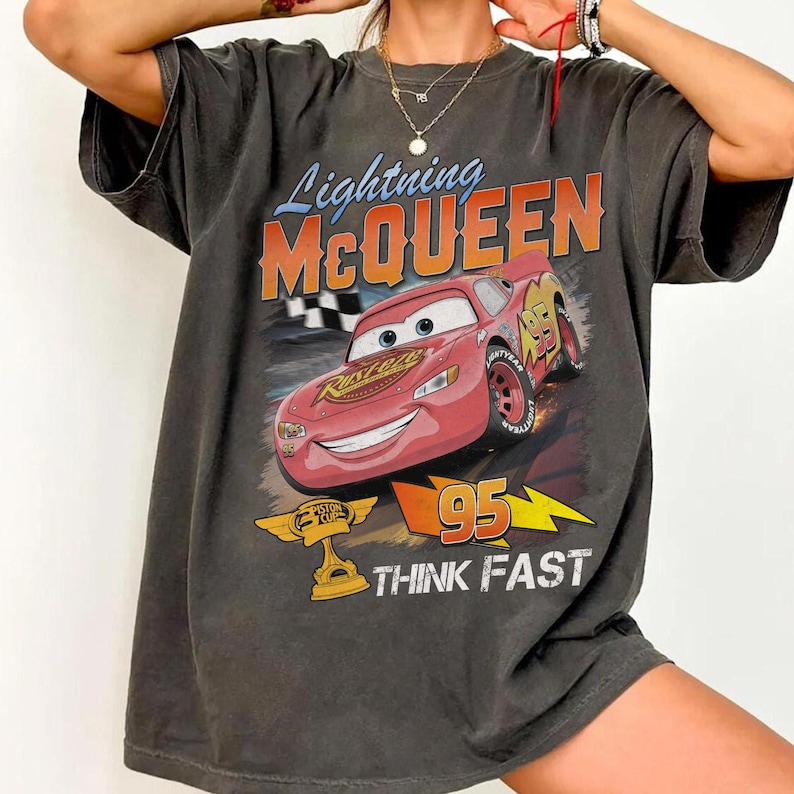 May include: Dark gray t-shirt featuring Lightning McQueen from the Cars movie. The graphic includes McQueen, the number 95, and the words "THINK FAST". The shirt has a vintage, distressed look.