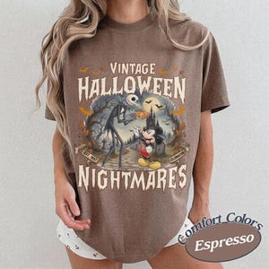 Puede incluir: Una camiseta marr&oacute;n de manga corta con un estampado gr&aacute;fico que incluye el texto VINTAGE HALLOWEEN NIGHTMARES. El dise&ntilde;o muestra una figura esquel&eacute;tica alta y un rat&oacute;n de dibujos animados frente a un castillo, rodeados de murci&eacute;lagos.