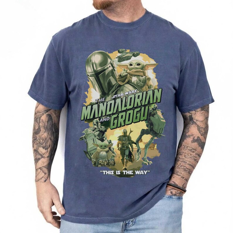 May include: Blue t-shirt featuring a graphic from "The Mandalorian" with the text "The Mandalorian and Grogu." The design includes images of the Mandalorian, Grogu, and other characters from the Star Wars series. The phrase "This is the Way" is also printed on the shirt.