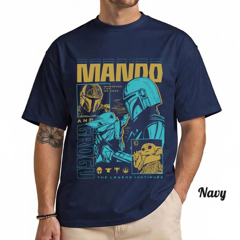 May include: A navy blue short-sleeve t-shirt featuring a graphic print of Mando and Grogu. The design includes the text MANDO AND GROGU, WHEREVER I GO, HE GOES, and THE LEGEND CONTINUES, with illustrations of the characters in blue and gold tones.