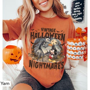 Puede incluir: Una camiseta color &ntilde;ame con un estampado gr&aacute;fico que incluye el texto VINTAGE HALLOWEEN NIGHTMARES, EST. 1937 y CELEBRATION. La ilustraci&oacute;n muestra una figura esquel&eacute;tica alta y un rat&oacute;n de dibujos animados en un cementerio con murci&eacute;lagos.
