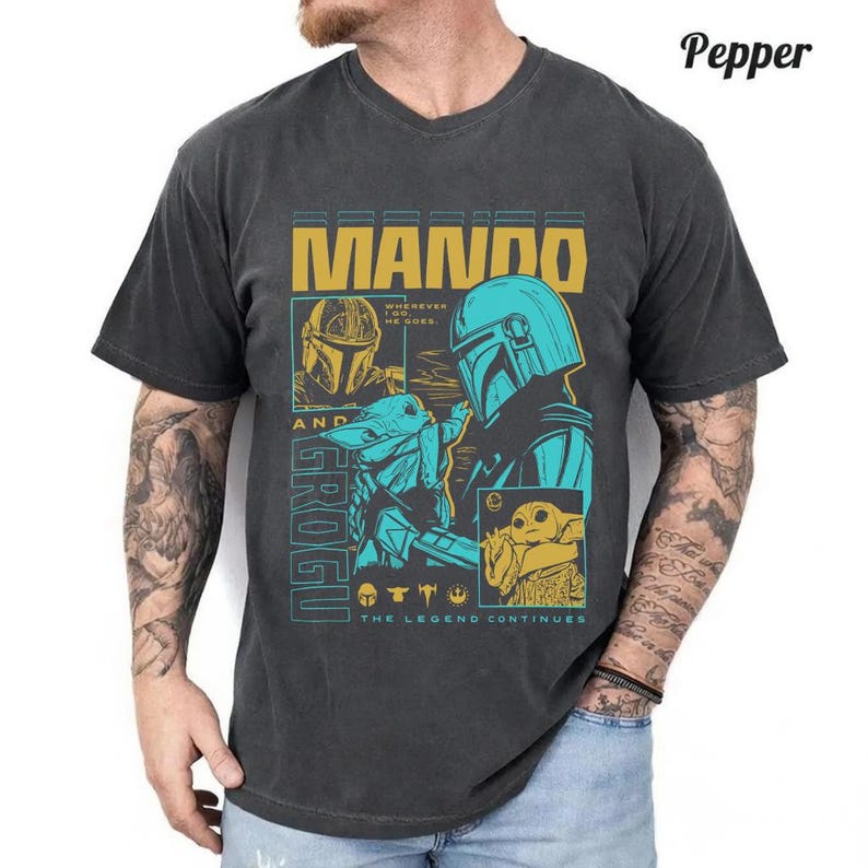 May include: A charcoal gray short-sleeve t-shirt featuring a graphic print of Mando and Grogu. The design includes the text MANDO, GROGU, WHEREVER I GO, HE GOES, and THE LEGEND CONTINUES, with yellow and teal illustrations of the characters.
