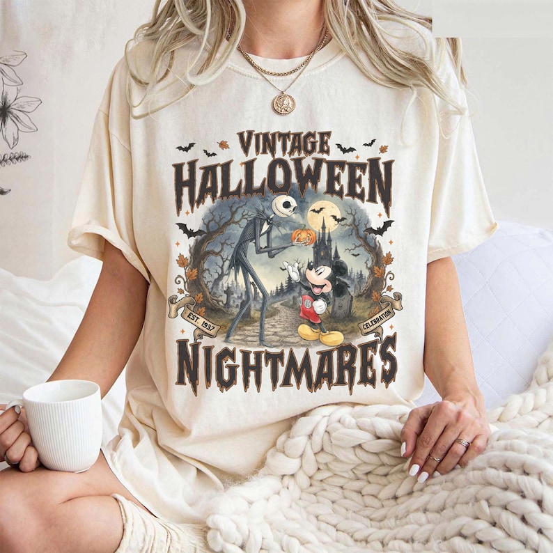 Puede incluir: Una camiseta de color crema con un estampado gr&aacute;fico que incluye el texto VINTAGE HALLOWEEN NIGHTMARES EST. 1937 CELEBRATION. El dise&ntilde;o muestra a Jack Skellington y Mickey Mouse en un bosque espeluznante con murci&eacute;lagos, un castillo y una luna llena.