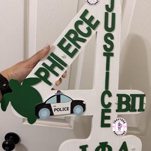 May include: White wooden number 4 with green lettering that reads "PHI ERCE", "JUSTICE", "ICE", and "I ΦΛ". A green turtle and a police car are also attached. The number is decorated with small pearls.