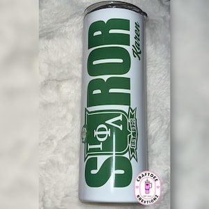 May include: A white insulated tumbler with a green design. The tumbler features the Greek letters Φ, Ρ, and a stylized emblem, along with the name "Karen" and the text "EST. 1929". The tumbler also has the text "SROR" in large green letters.