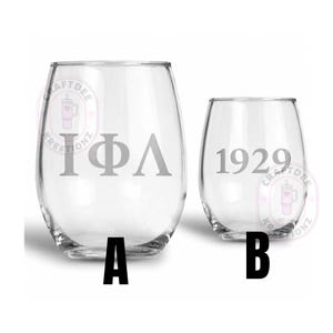 May include: Two clear stemless wine glasses labeled A and B. Glass A features the Greek letters Iota Phi Lambda in a light grey font. Glass B displays the number 1929 in a matching light grey font. Both glasses have a rounded, smooth shape.