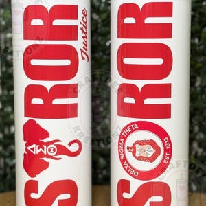 May include: Two white insulated tumblers with red text and graphics. One tumbler features the word "SROR" and an elephant graphic. The other tumbler has "SROR" and a sorority crest. The word "Justice" is written vertically.