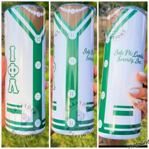 May include: A white tumbler with a green and brown design resembling a shirt. The tumbler features the Greek letters IΦΛ, buttons, and the text "Iota Phi Lambda Sorority, Inc."