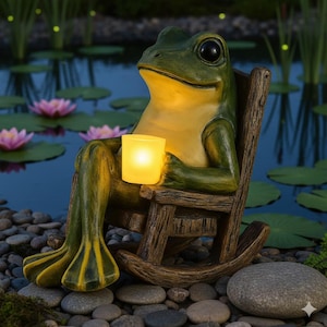 Puede incluir: Una estatua de rana caprichosa en una mecedora, sosteniendo una vela encendida. La rana es verde y amarilla, con grandes ojos negros. La silla es de madera envejecida. La escena está ambientada junto a un estanque con nenúfares y flores rosas.