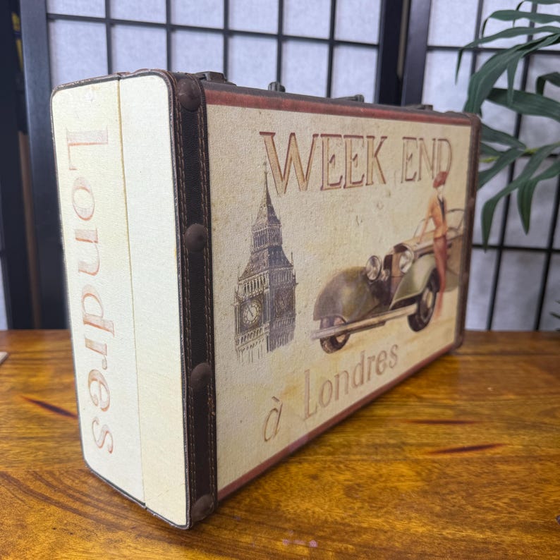 May include: A vintage-style decorative suitcase with the words "Week End &agrave; Londres" printed on the front. The suitcase features an illustration of Big Ben and a classic car. The sides of the suitcase are cream-colored with the word "Londres" printed vertically.