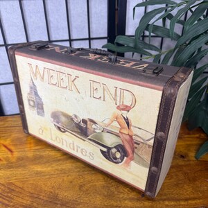 May include: Vintage-style decorative suitcase with a cream-colored background. The suitcase features the words "WEEK END" and "&agrave; Londres" with an illustration of a woman and a classic car. The suitcase has brown trim and metal hardware.