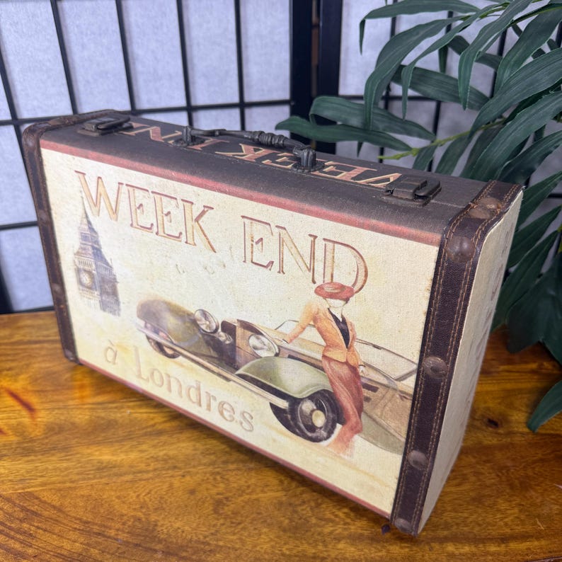 May include: Vintage-style decorative suitcase with a cream-colored background. The suitcase features the words "WEEK END" and "&agrave; Londres" with an illustration of a woman and a classic car. The suitcase has brown trim and metal hardware.