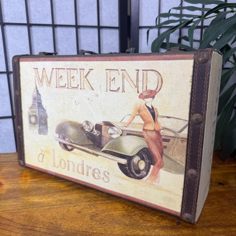 May include: A vintage-style decorative suitcase with a cream-colored front panel. The panel features an illustration of a woman in a suit next to a classic car, with the text "WEEK END &agrave; Londres" and a Big Ben image.