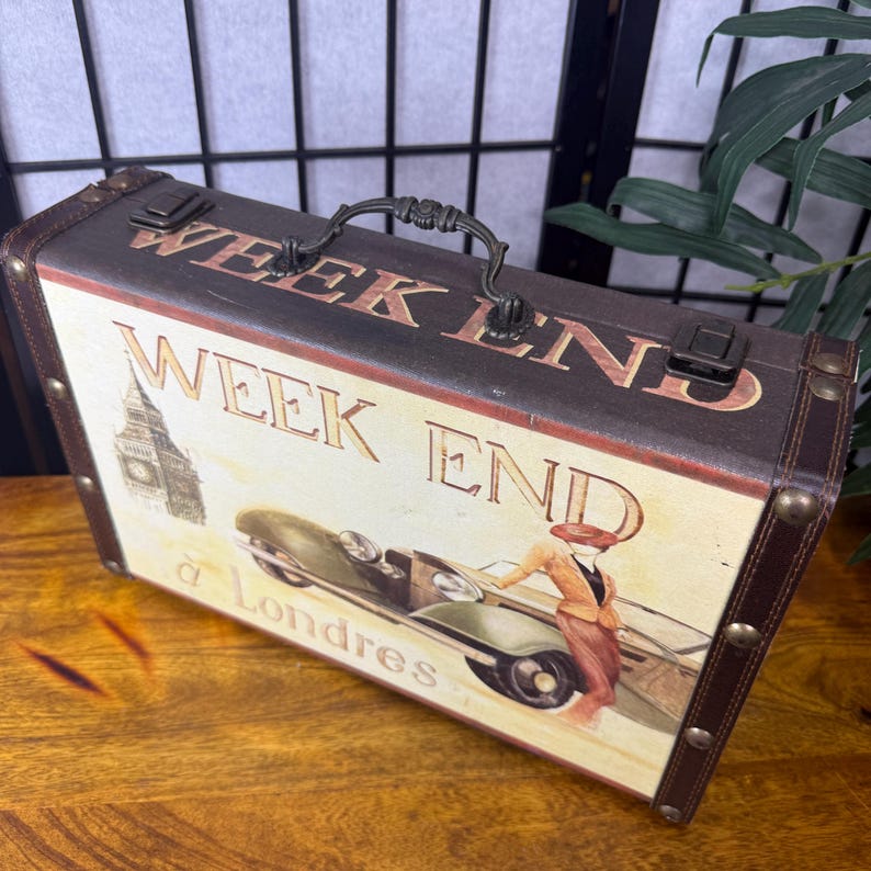 May include: A decorative wooden suitcase with the words "WEEK END" in brown lettering. The suitcase features an illustration of a vintage car and a person in a hat, with the text "&agrave; Londres". The suitcase has a brown handle and metal accents.