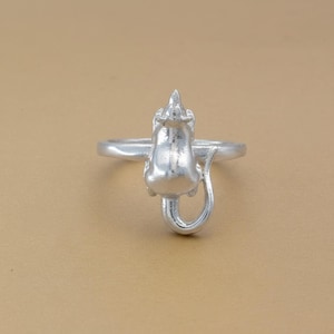 May include: A silver-colored ring featuring a detailed mouse design. The mouse is depicted in a standing position with its tail curled. The ring has a smooth, polished finish and is set against a neutral background.