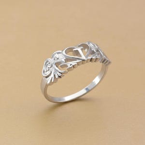 以下が含まれることがあります： ハートと花の要素を特徴とする装飾的なデザインのシルバーリング。 リングは繊細な透かし模様と磨かれた仕上げが施されています。 リングはジュエリーです。