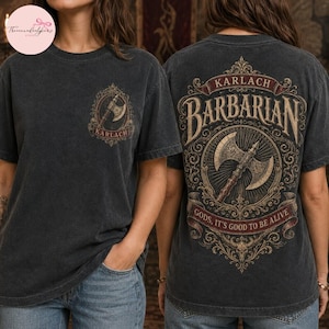 May include: A charcoal gray t-shirt featuring a small graphic on the front chest of an axe inside an ornate frame with the text KARLACH. The back displays a large, detailed graphic of a double-headed axe with the text KARLACH BARBARIAN.