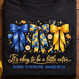 May include: Black t-shirt with three decorative bows in blue and yellow, with puzzle piece patterns. The text reads "It's okay to be a little extra. DOWN SYNDROME AWARENESS."