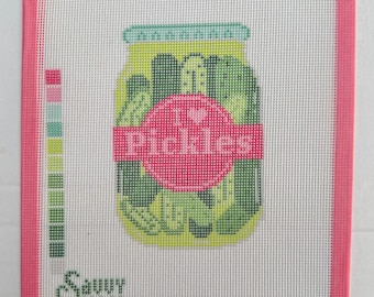 May include: A needlepoint canvas featuring a jar of green pickles with a pink label that reads I heart Pickles. The design includes a color palette guide on the left side and the text Savvy Stitch in the bottom left corner, all framed by a pink border.