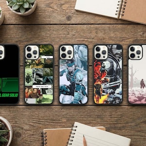 May include: A collection of five phone cases featuring designs inspired by the video game Metal Gear Solid. The cases display various graphics, including character illustrations and the game's logo in green and black. The cases are arranged on a wooden surface.