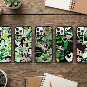 May include: Five phone cases with green and black designs featuring cartoon characters. The cases have different patterns, including floral, collage, and character portraits. The cases are on a wooden surface with plants and notebooks.