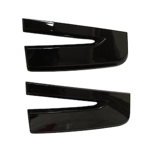 Pode incluir: Duas peças de acabamento automotivo idênticas em preto brilhante, cada uma apresentando um design distinto com um recorte em forma de V. Estes componentes possuem uma superfície lisa e reflexiva e uma forma curva e alongada.