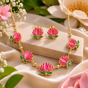 May include: A gold-toned necklace and matching stud earrings set featuring pink and green enamel lotus flower motifs. The necklace chain is interspersed with small gold beads, and each lotus flower is detailed with vibrant pink petals and green leaves.