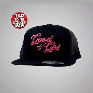 May include: Black trucker hat with a curved brim and mesh back. The front of the hat features the embroidered words "Good Girl" in pink script with a heart symbol. A red and white circular graphic is in the upper left corner.