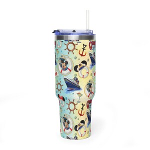 May include: A tall stainless steel tumbler with a clear lid and straw, featuring a light blue and yellow background patterned with cruise ships, brown ship wheels, red anchors, life preservers, and cartoon mouse ears in sailor hats.