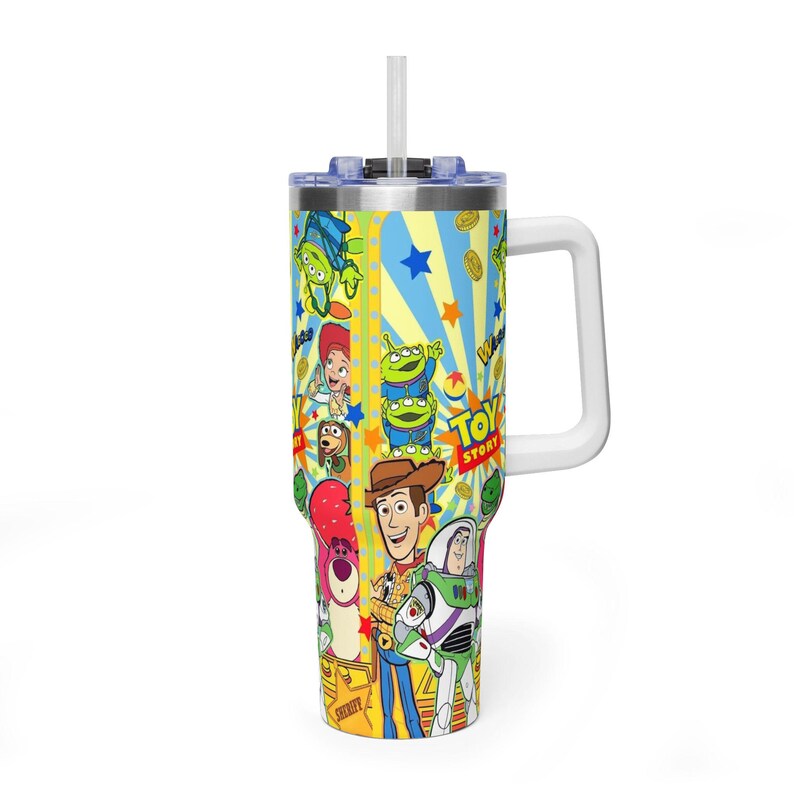 May include: An insulated tumbler with a vibrant "Toy Story" design. The tumbler has a white handle, a blue lid, and a white straw. The design features Woody, Buzz Lightyear, and other characters from the film. The tumbler is suitable for cold drinks.