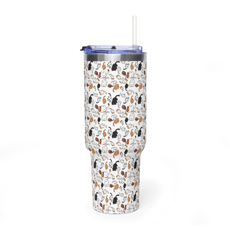 Op de afbeelding: Een witte beker met een blauw deksel en een doorzichtig rietje. De beker heeft een herhalend patroon van zwarte, bruine en oranje kattenillustraties. Ontworpen voor koude dranken.