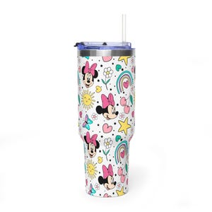Puede incluir: Un vaso blanco con un patr&oacute;n colorido que presenta a Minnie Mouse, arco&iacute;ris, estrellas, flores, mariposas y corazones. El vaso tiene una tapa azul y una pajita transparente. El dise&ntilde;o es alegre y brillante.