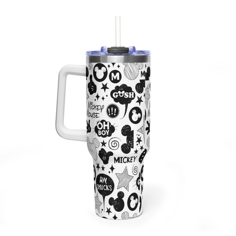 May include: A white tumbler with a black and white Mickey Mouse themed design. The tumbler features a handle, a lid, and a straw. The design includes Mickey Mouse icons, stars, and speech bubbles with phrases like "Gush" and "Oh Boy".