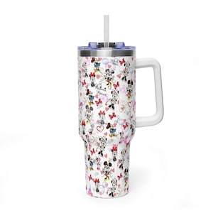 Puede incluir: Vaso blanco con asa y pajita, con un estampado repetido de ilustraciones de Minnie Mouse, corazones y lazos. El vaso tiene una tapa azul y un asa blanca. El texto "Minnie Mouse" es visible.