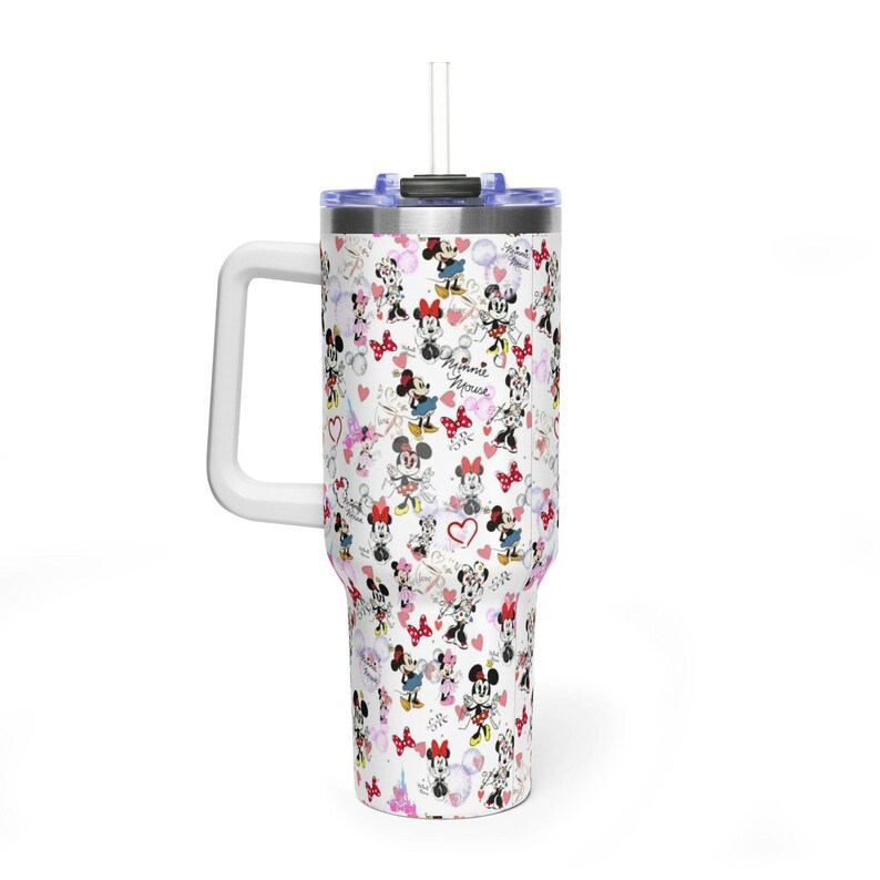 Puede incluir: Un vaso blanco con asa y pajita, cubierto con un estampado de personajes de Minnie Mouse, corazones y lazos. El texto "Minnie Mouse" tambi&eacute;n es visible. El vaso tiene un asa blanca y una tapa azul.