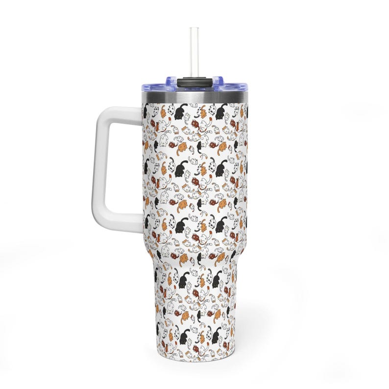 Op de afbeelding: Een witte beker met een handvat en een rietje. De beker is bedekt met een herhalend patroon van zwarte, oranje en witte kattenillustraties. Het deksel is blauw en het handvat is wit.
