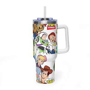 May include: White tumbler featuring a colorful collage of Toy Story characters. The tumbler has a white handle, a blue lid, and a clear straw. The words "Toy Story" are visible on the tumbler.