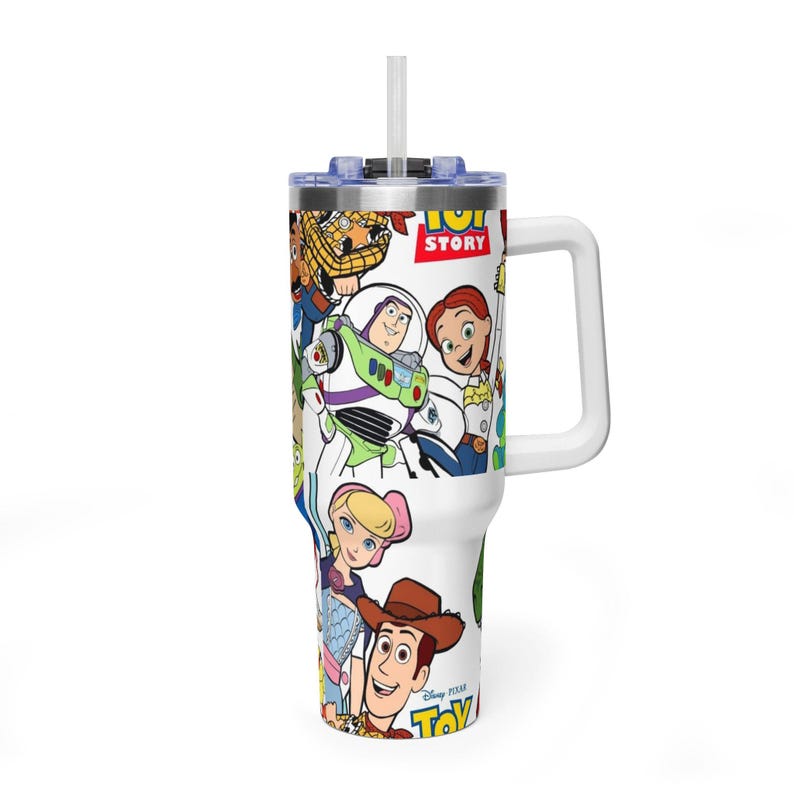 May include: White tumbler featuring a colorful collage of Toy Story characters. The tumbler has a white handle, a blue lid, and a clear straw. The words "Toy Story" are visible on the tumbler.