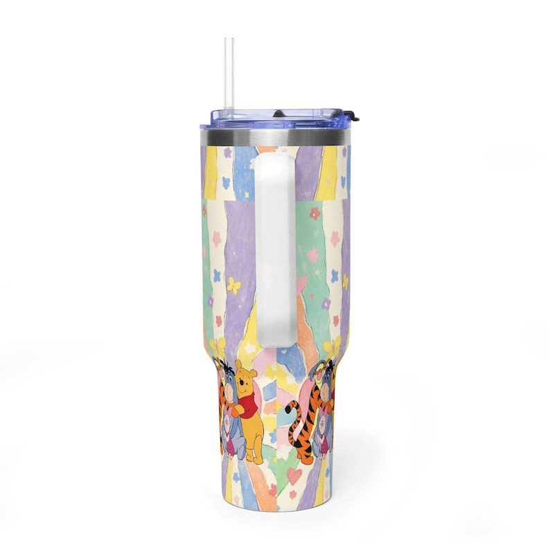 Puede incluir: Un vaso de acero inoxidable con asa, tapa transparente y pajita. El exterior presenta un patr&oacute;n de rayas verticales en colores pastel con peque&ntilde;as flores, mariposas y corazones, junto con ilustraciones de Winnie the Pooh, Igor y Tigger.