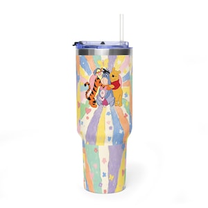 Puede incluir: Un vaso de acero inoxidable con tapa transparente y pajita, con un fondo de arco&iacute;ris en tonos pastel con peque&ntilde;os corazones y mariposas. El centro muestra una ilustraci&oacute;n de Winnie the Pooh, Tigger, Igor y Piglet d&aacute;ndose un abrazo.