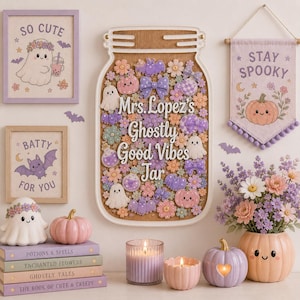 Puede incluir: Un letrero de pared con forma de frasco con el texto Mrs. Lopez's Ghostly Good Vibes Jar, rodeado de pequeños recortes de fantasmas, calabazas, murciélagos y flores. La decoración incluye cuadros, libros apilados, velas y figuras de calabaza.