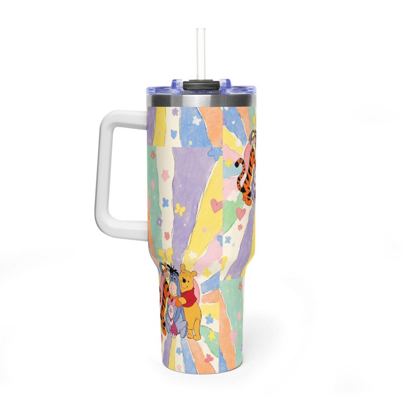 Puede incluir: Un vaso de acero inoxidable con asa y pajita transparente, que presenta un patr&oacute;n de rayos de sol en tonos pastel con ilustraciones de Winnie the Pooh, Igor y Tigger, decorado con peque&ntilde;as flores, mariposas y corazones en la superficie.
