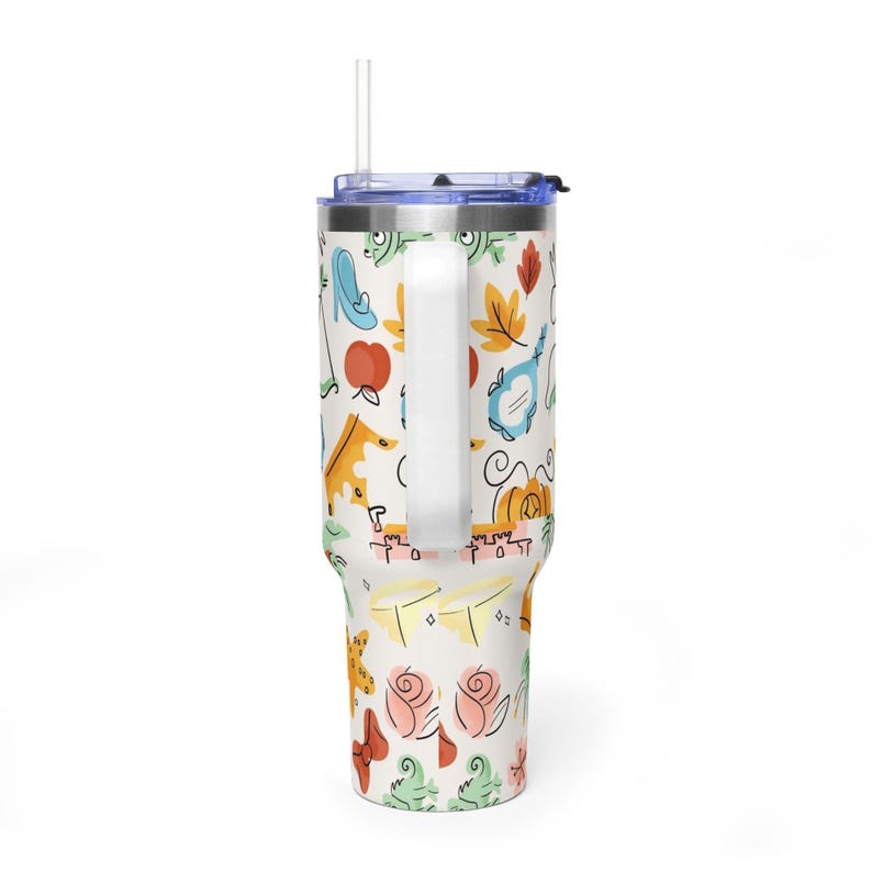 May include: White travel mug with a blue lid and handle, featuring a whimsical pattern of cartoon illustrations. The design includes a high-heeled shoe, an apple, a mirror, a pumpkin, and roses. A clear straw extends from the lid.