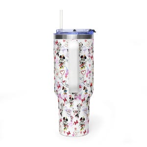 Puede incluir: Un vaso blanco con asa, con un estampado de personajes de Minnie Mouse, corazones y globos. El vaso tiene una tapa azul y una pajita transparente. El dise&ntilde;o incluye detalles en rojo, rosa y negro.