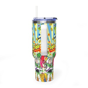 May include: A vibrant tumbler with a design from the film "Toy Story." The design includes Buzz Lightyear, Woody, and other characters, with the words "Toy Story" in a bold font. The tumbler has a white handle and a straw.
