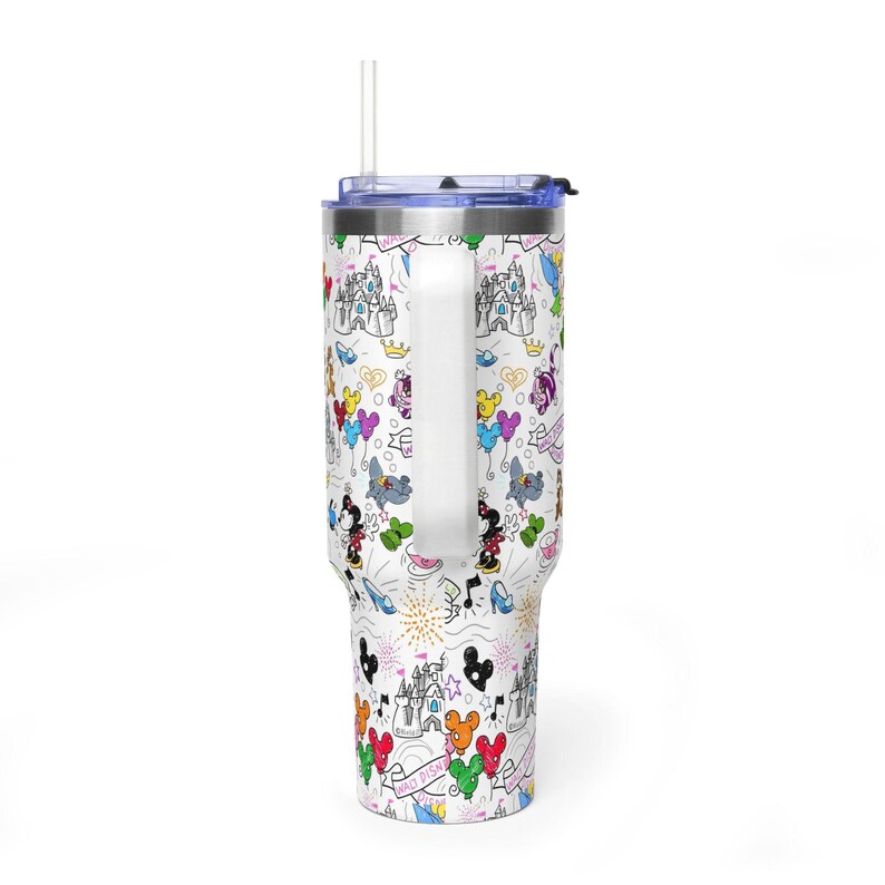 Puede incluir: Vaso blanco con asa, con un colorido dise&ntilde;o tem&aacute;tico de Disney. El dise&ntilde;o incluye personajes de dibujos animados, castillos, globos y fuegos artificiales. El vaso tiene una tapa azul y una pajita transparente.