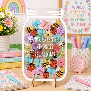 May include: A clear jar-shaped reward system with a wooden stand, filled with colorful insect and flower-shaped tokens. The jar reads "MRS. GREEN'S KINDNESS REWARD JAR". Decorative elements include a rainbow, flowers, and pens.