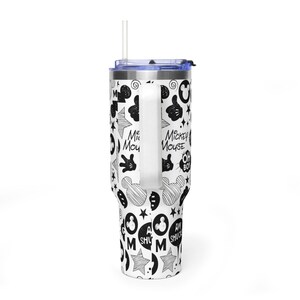 May include: White tumbler with a black and white Mickey Mouse pattern. The design includes Mickey Mouse hands, stars, and text. It has a handle, a blue lid, and a clear straw. The tumbler is designed to keep drinks cold or hot.