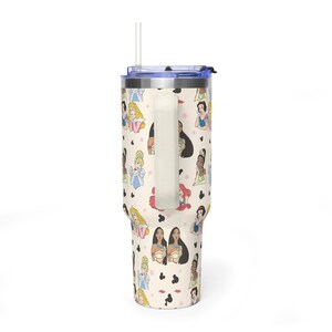 K&ouml;nnte beinhalten: Ein cremefarbener Becher mit einem Muster aus Cartoon-Prinzessinnen und schwarzen Mickey-Mouse-f&ouml;rmigen Symbolen. Der Becher hat einen wei&szlig;en Griff, einen blauen Deckel und einen durchsichtigen Strohhalm. Das Design umfasst Illustrationen verschiedener Prinzessinnen.