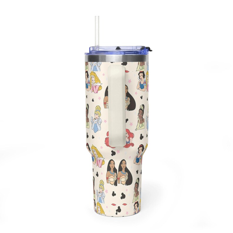 K&ouml;nnte beinhalten: Ein cremefarbener Becher mit einem Muster aus Cartoon-Prinzessinnen und schwarzen Mickey-Mouse-f&ouml;rmigen Symbolen. Der Becher hat einen wei&szlig;en Griff, einen blauen Deckel und einen durchsichtigen Strohhalm. Das Design umfasst Illustrationen verschiedener Prinzessinnen.